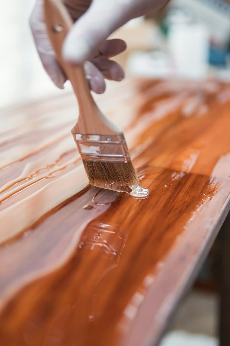 Brushing a coat of clear polyurethane onto a wooden tabletop