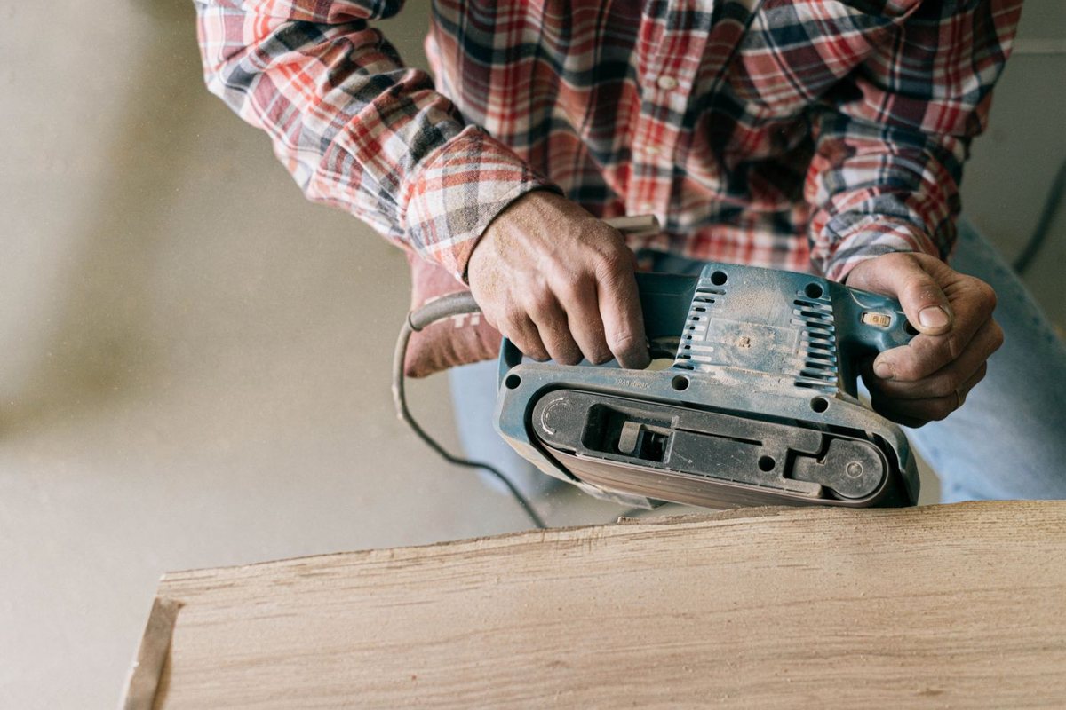 Handheld belt sander leveling a rough wooden board
