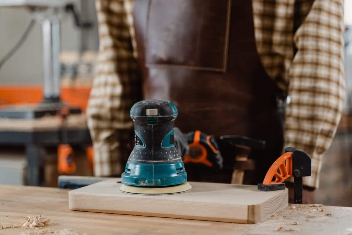 Random orbital sander resting on a board in a woodworking shop