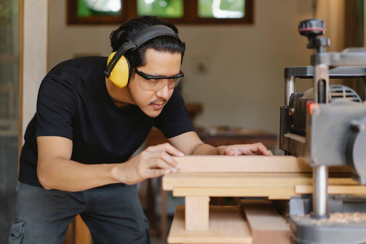 Woodworker in ear and eye protection feeding a board into a benchtop thickness planer