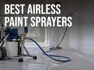 Best airless paint sprayer in use: a painter spraying white paint on a living room wall with a stand-mounted airless sprayer and hose