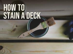 How to stain a deck: an open can of stain with a natural-bristle brush on bare deck boards